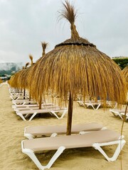 Straw umbrellas and beach sunbeds on sand, Cloudy overcast day at the empty sea beach. Summer vacation is over. off season, no people