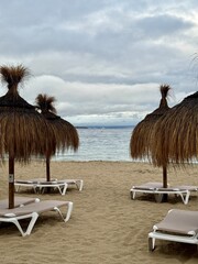 Straw umbrellas and beach sunbeds on sand, Cloudy overcast day at the empty sea beach. Summer vacation is over. off season, no people