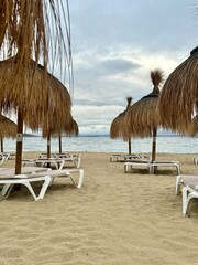 Straw umbrellas and beach sunbeds on sand, Cloudy overcast day at the empty sea beach. Summer vacation is over. off season, no people