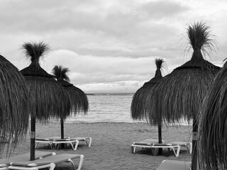 Straw umbrellas and beach sunbeds on sand, Cloudy overcast day at the empty sea beach. Summer...