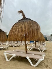 Straw umbrellas and beach sunbeds on sand, Cloudy overcast day at the empty sea beach. Summer vacation is over. off season, no people