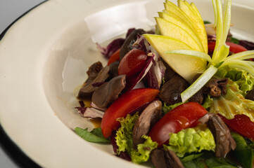 Gourmet salad featuring chicken or duck liver, mixed greens, cherry tomatoes, and fan-cut yellow apple, served on an ivory-colored restaurant plate