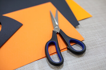 Pair of scissors lying on black and orange craft paper, surrounded by cutouts, representing creative paper crafts or halloween themes