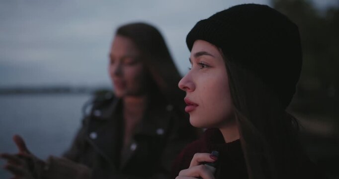 A woman smokes an electronic cigarette near a lake standing with her friend