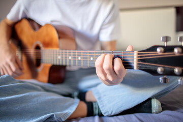 Close-up of a person's hands strumming and pressing chords on the neck of an acoustic guitar while sitting and practicing