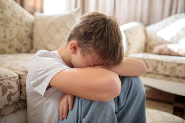 Sad and depressed teenage boy sitting on the floor with his head buried in his arms, expressing...