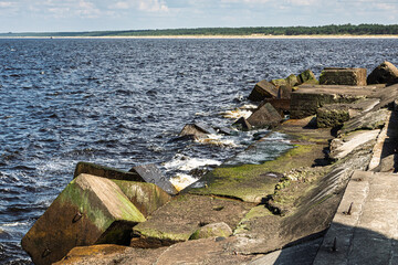 Concrete breakwater on the seashore, waves hitting the blocks