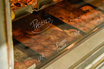 A close-up shot of freshly baked Pastizzi with a Ricotta Cheese filling, clearly labeled in a warmly lit glass bakery display case. Focus on the flaky texture of the traditional Maltese pastry.