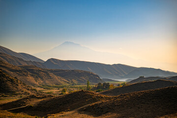 A mountain range with a lake in the distance. The sky is clear and the sun is setting