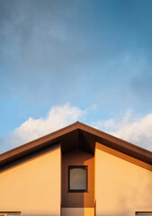 The gable end of a house with a recessed window. Detail of modern countryside house at sunset, cloudy house in the background.