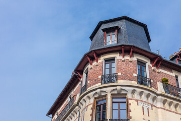 Charming early 20th-century building in Rennes with brick and stone fa ade, wrought iron balconies, and a mansard roof. The architecture stands out against a clear blue sky, showcasing elegant French