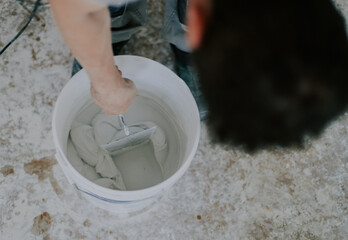 A young man mixes putty with a construction spatula in a bucket.