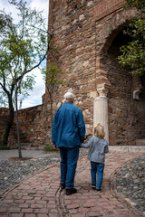 Grandfather and grandson walking hand in hand through ancient ruins, with columns and brick walls in the background
