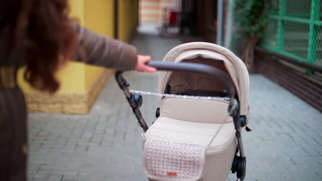 Close up of a hand pushing a beige baby stroller while walking through a colorful urban street