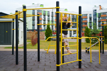 child playing on jungle gym at outdoor playground surrounded by modern urban housing. active lifestyle, childhood fun, healthy recreation in city environment. autumn day, casual outfit