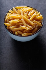 Dry Yellow Penne Pasta in Ceramic Bowl on Dark Background