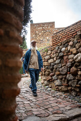 Elderly man walking through a historic stone pathway, framed by ancient brick walls