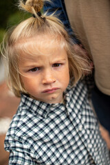 A close-up of a young child with a serious expression, wearing a checkered shirt, showing freckles and intense eyes