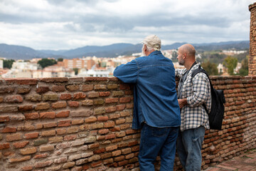 Two men enjoying the view from a historic fortress wall, looking out over the city and mountains