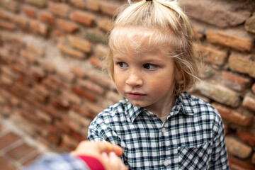 Close-up of a child with freckles smiling and shaking hands, against a brick wall background