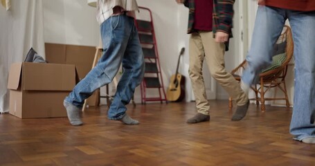 Friends in jeans dancing on the floor after Happy moving into a new apartment with cardboard boxes and housewarming party