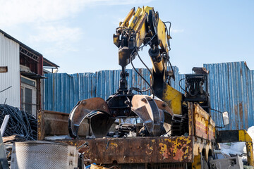 Mobile lifting crane handling scrap metal cargo. Mobile crane truck bed. Scrap yard crane placing rusty metal into truck.
