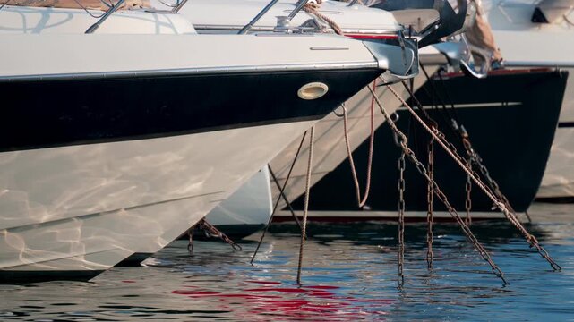 Close up of ropes and metal chains securing a luxury yacht in port, with blurred water and boats in the background