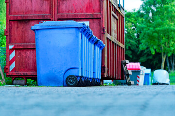 Row of blue garbage bins beside large industrial metal skip
