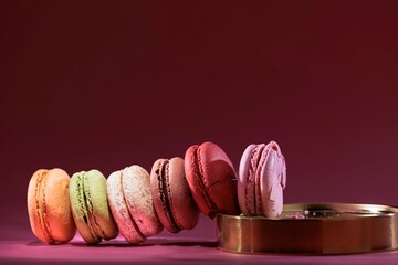 A row of vibrant macarons in orange, green, cream, brown, red and pink are arranged along the edge...