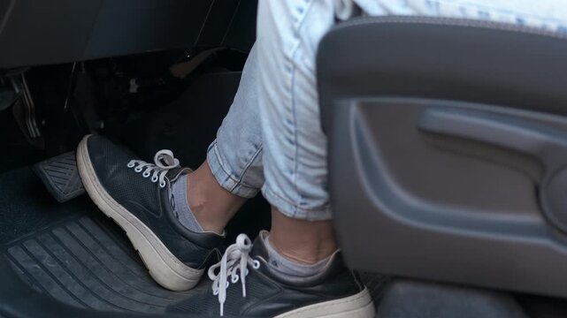Driver foot pressing pedal in car. Female driver repeatedly pressing car pedal during driving lesson, focusing on foot movement and vehicle control while wearing sneakers and jeans