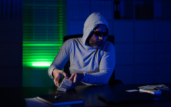 Burglar with stolen money. Thief stolen money from office in night robbery. A hooded bandit to steal cash. Crime scene with burglary. Robber in hoodie stolen money. Stolen money concept.