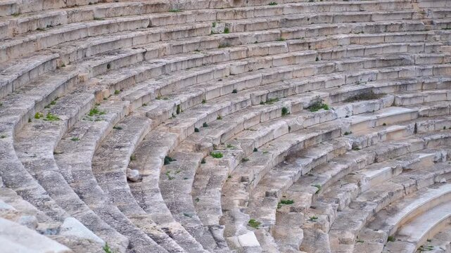 Ancient stone steps of amphitheater sweeping pan. Smooth camera movement showcasing the weathered stone steps of the ancient amphitheater, revealing its historical grandeur and architectural design