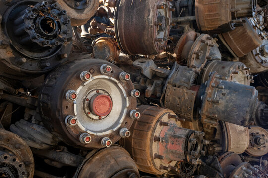 Old rusty truck axles piled in a scrap yard. Discarded heavy truck parts in metal recycling area. Truck axle scrap metal waiting for recycling.