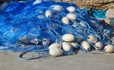 Blue fishing net tangled with white floats lies on the ground, showcasing the intricate details of fishing gear and the vibrant colors of the materials used in marine activities and fishing practices © Izi18