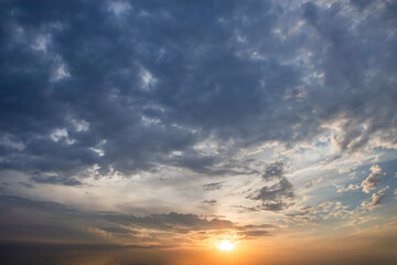 Obraz premium Sky showing a vibrant sunset with a large area of dark, full clouds at the top and brighter, more varied clouds illuminated by the setting sun casting an orange glow closer to the horizon