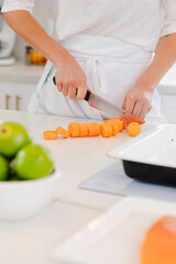 Woman's hands chopping carrots on a white kitchen counter for healthy cooking and meal preparation