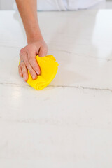 Hand wiping kitchen counter with yellow microfiber cloth, cleaning marble surface for hygiene