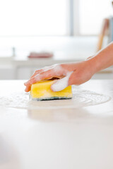 Hand holding a yellow sponge saturated with soap and foam, wiping clean a bright white surface in a kitchen