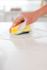 Hand using sponge with foam for cleaning kitchen countertop, scrubbing surface for hygiene and housework