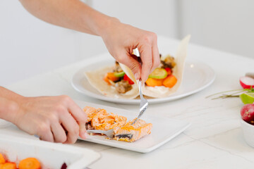 Hands preparing healthy fish tacos for lunch, flaking baked salmon and adding toppings to tortillas