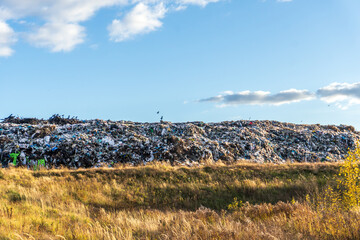 Large landfill site near a grassy area in bright daylight with scattered clouds and a clear blue sky
