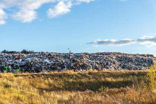 Large landfill site near a grassy area in bright daylight with scattered clouds and a clear blue sky