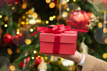 Man hand holding red gift box or present against Christmas tree. Xmas shopping. Boxing Day. Close up.