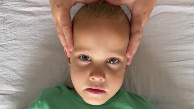 Close view of child face lying on couch during osteopathy treatment. Doctor places one hand on forehead and another on nose bridge, holding cranial points to release tension and improve breathing.