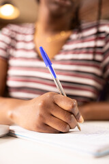 Selective focus on hand of female employee using pen to write down marketing strategy ideas on notepad. Close up of self employed black woman planning work schedule at home office desk.