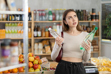 Female buyer carefully reads labels on water bottles - she chooses the best product in the...