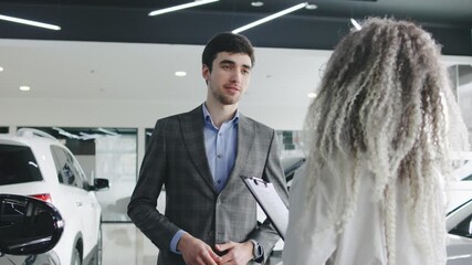 After a friendly conversation, a cheerful woman with curly hair seals the deal with a handshake and beams with joy, likely having just sold a car