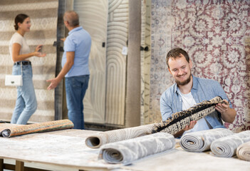 Fototapeta premium Young man buyer choosing soft rolled carpet in hardware store