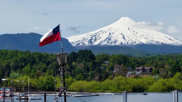 Close-up of the Chilean flag waving in the port of the city of Puc&oacute;n, with the imposing Villarrica volcano in the background.