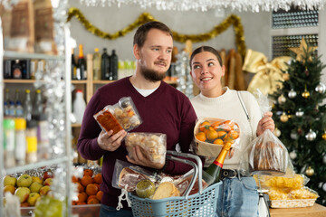Joyful husband and wife choose and buy nougat, panettone, marzipan, panellets together in grocery department of supermarket